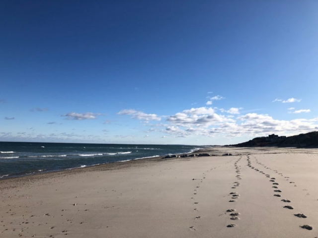 Two sets of footprints on the beach, blue sky with a few white clouds
